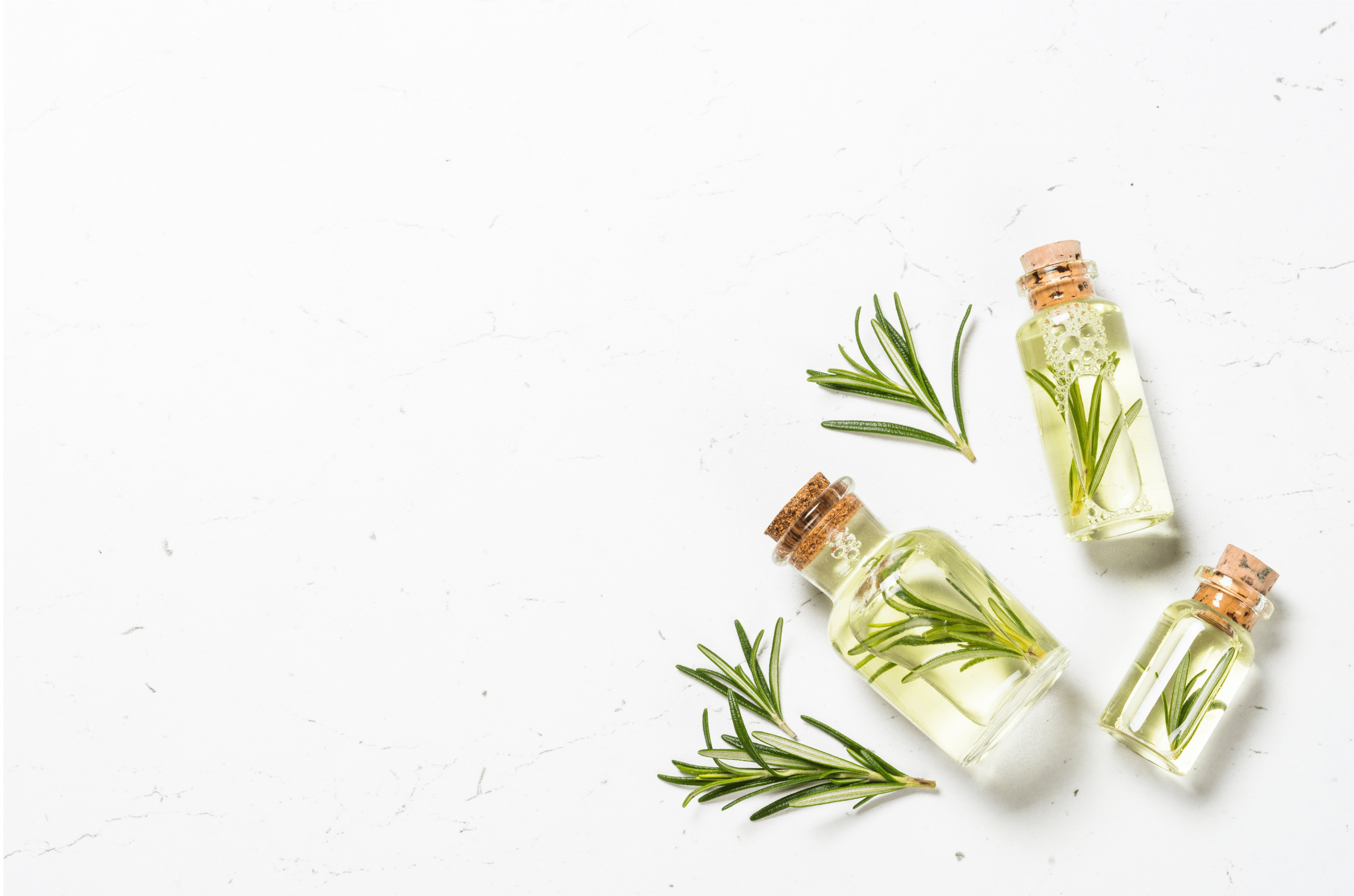 Small oil bottles with oil essence next to herbs on marble table